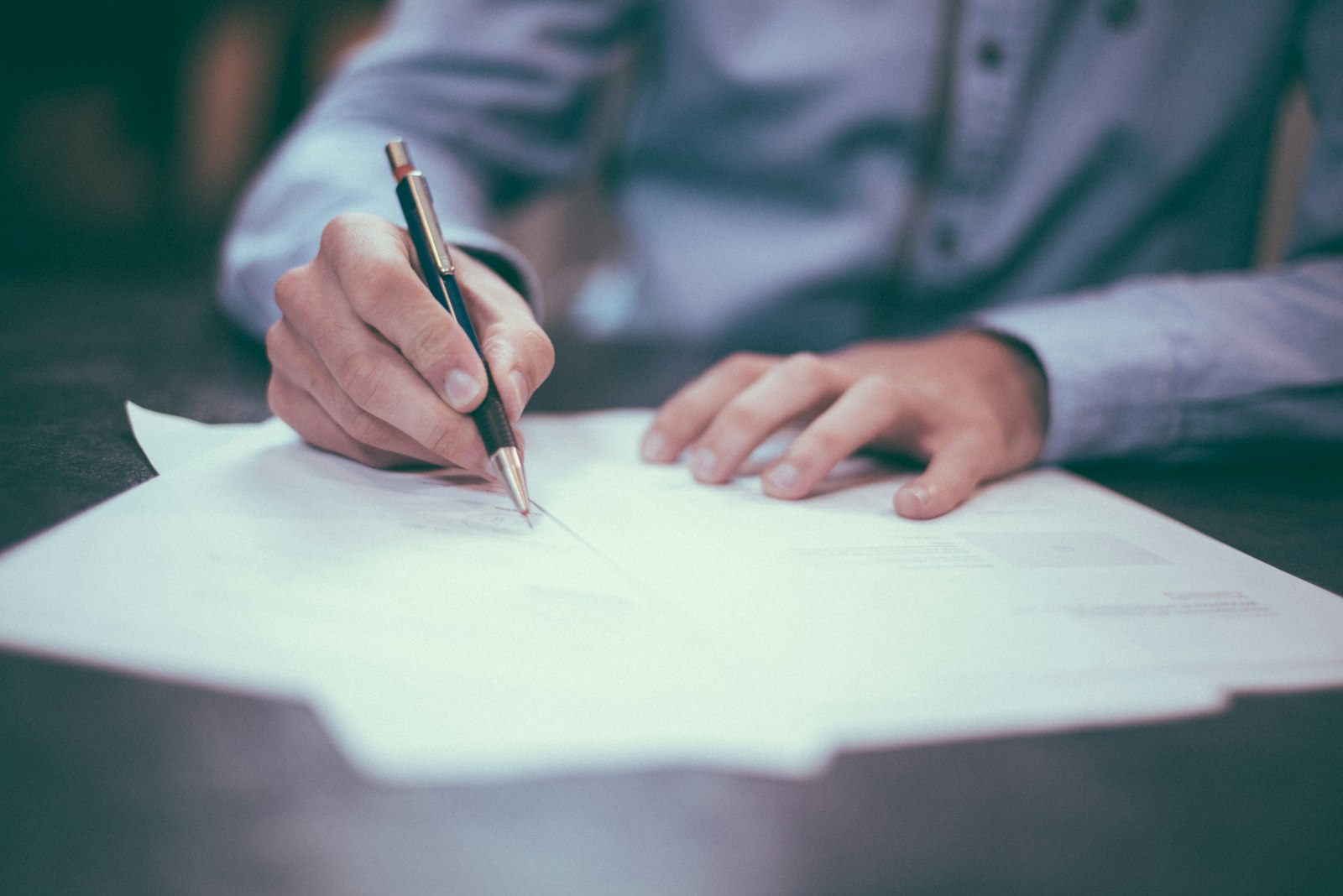 Two people signing business documents across a desk