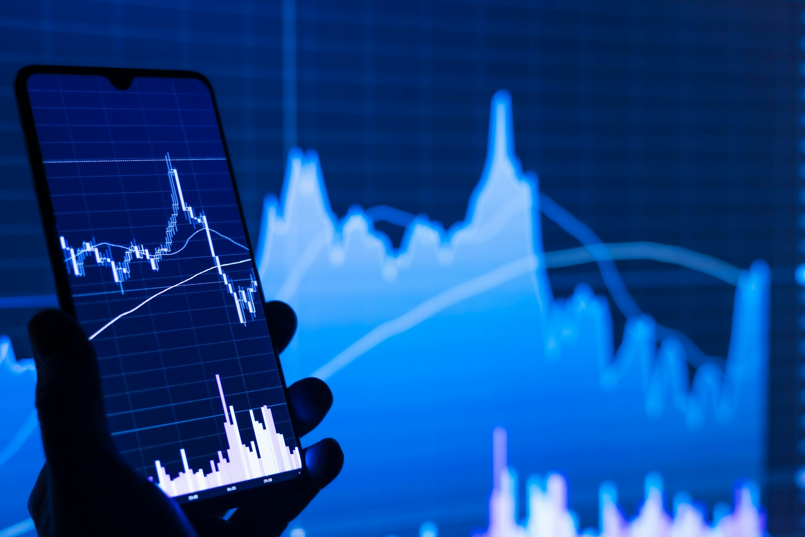 A hand holding a smartphone running a stock trading app with a price chart on screen